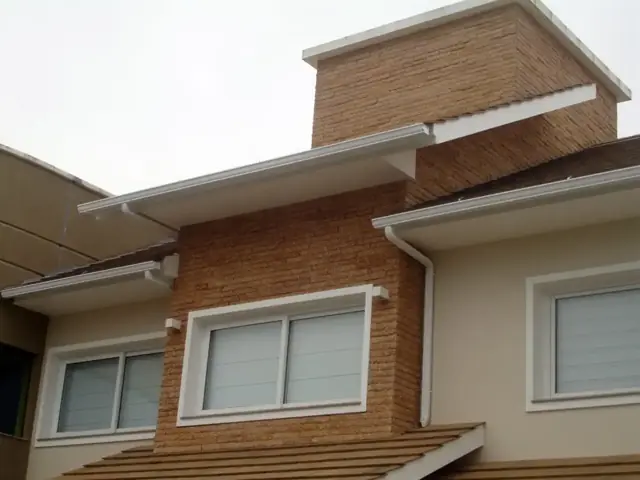 Sobrado com fachada de tijolo e calha branca nos dois beirais